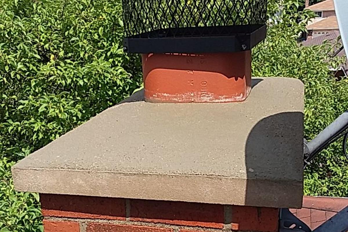 A brick chimney with a concrete crown and a black metal cap