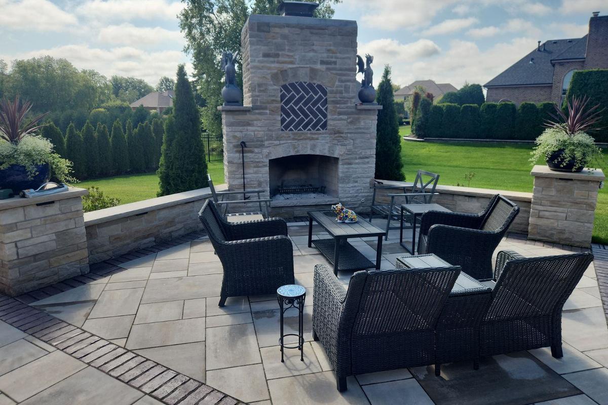 A stone outdoor fireplace on a paver patio with a seat wall, built by WJC Construction