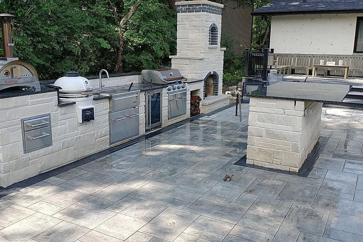 A stone outdoor kitchen with grills, a bar island and a fireplace, built by WJC Construction